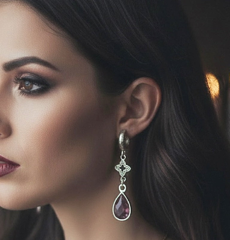 Luxe Amethyst Droplet Earrings.  Chunky silver hoops with a silver clover charm and an Amethyst teardrop crystal. Worn by a model on a dark background.
