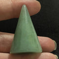 Green triangular stone held between fingers against a dark background