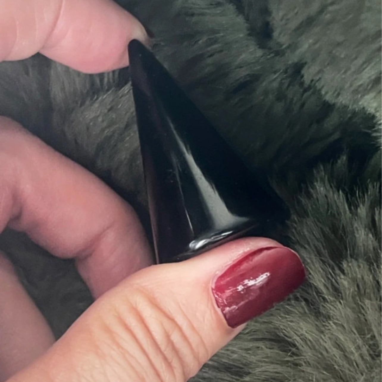 Black cone-shaped object held between fingers against a textured gray background