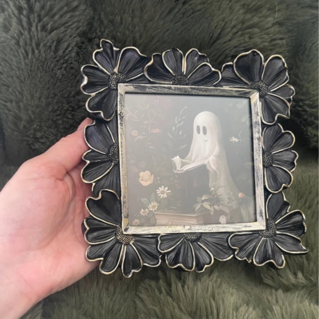 Decorative black floral photo frame held by a hand on a green textured background