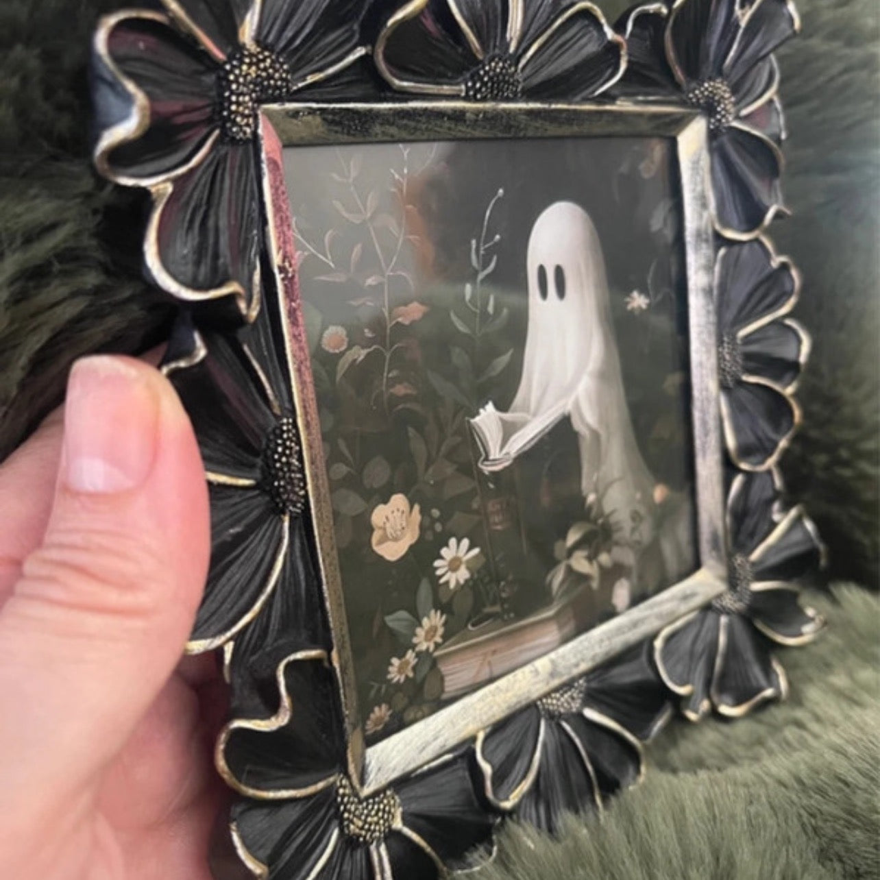 Decorative photo frame with a ghostly figure holding a book and flowers on a dark background.