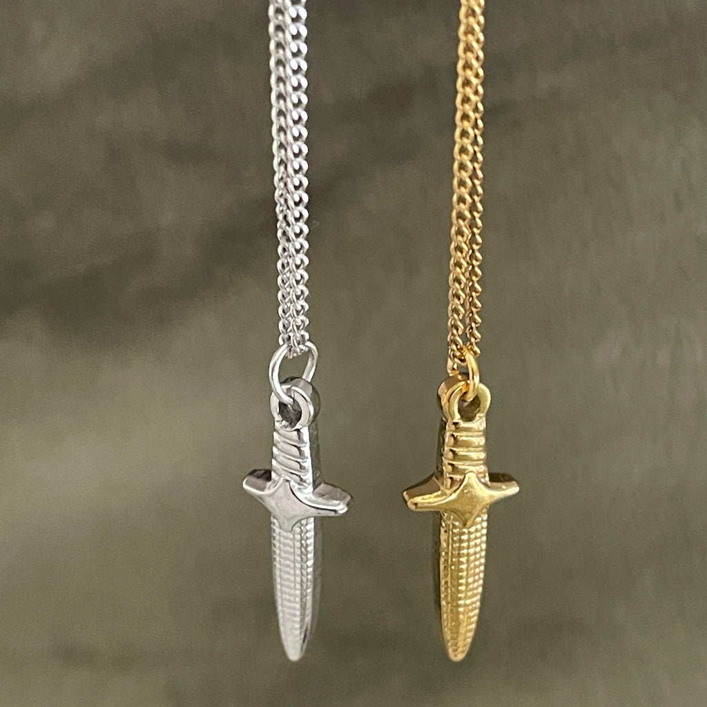 Silver and gold dagger-shaped pendants on chains against a textured brown background
