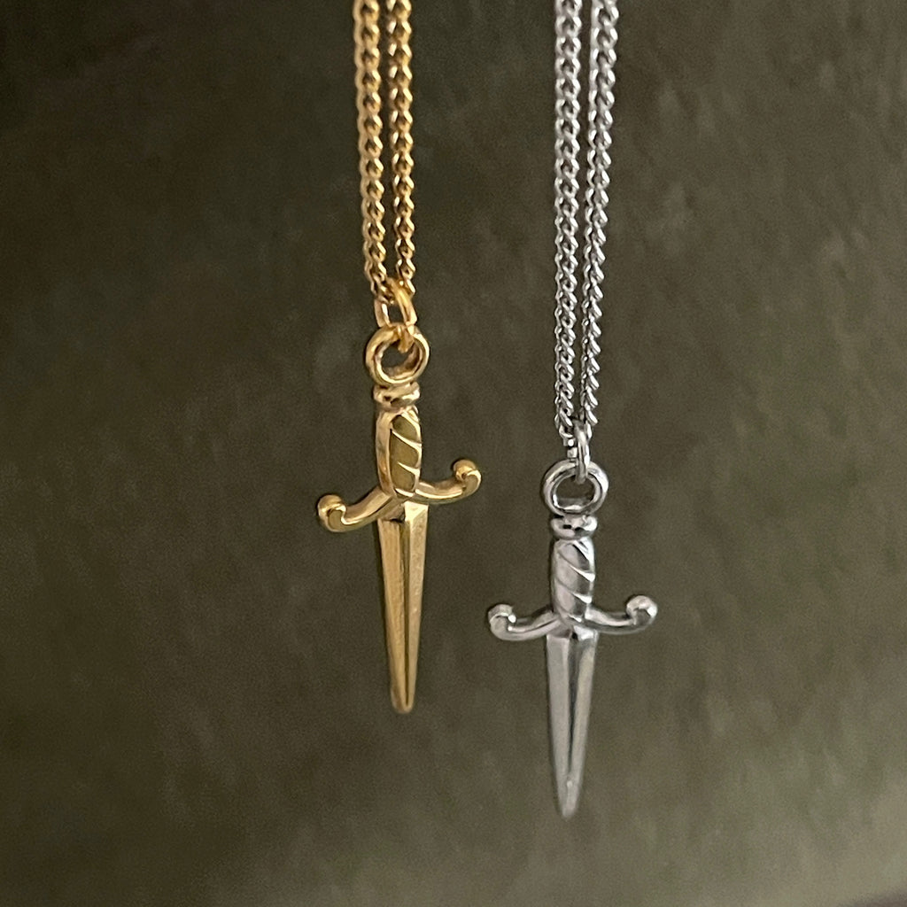 Gold and silver sword-shaped pendants on chains against a dark background