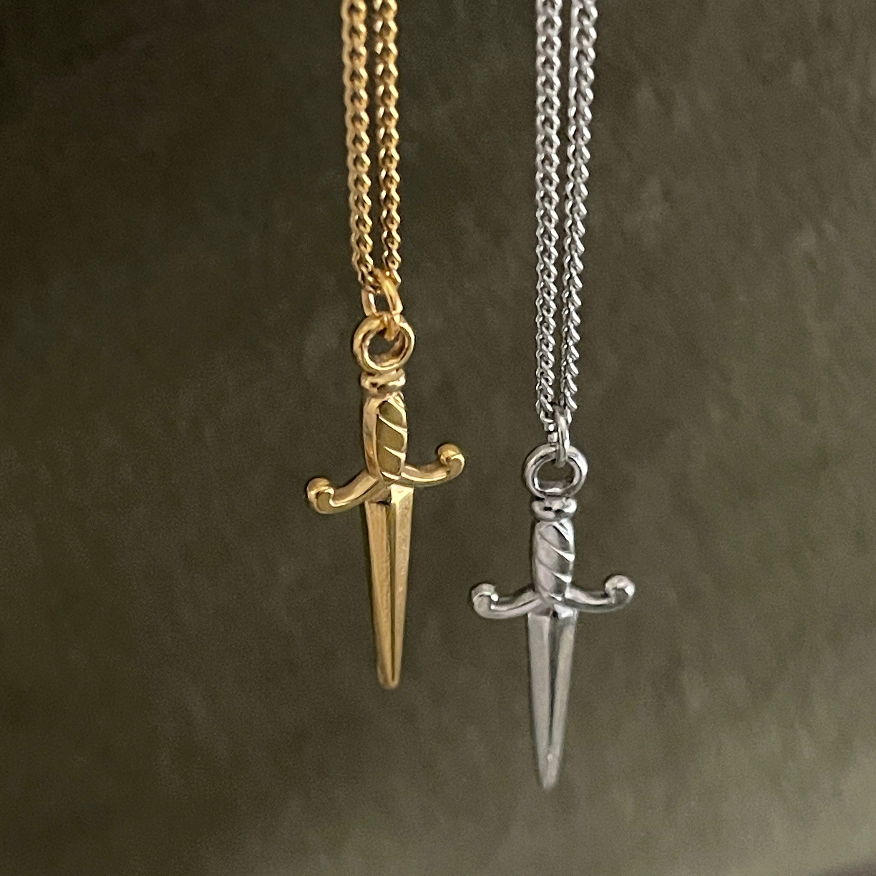 Gold and silver sword-shaped pendants on chains against a dark background