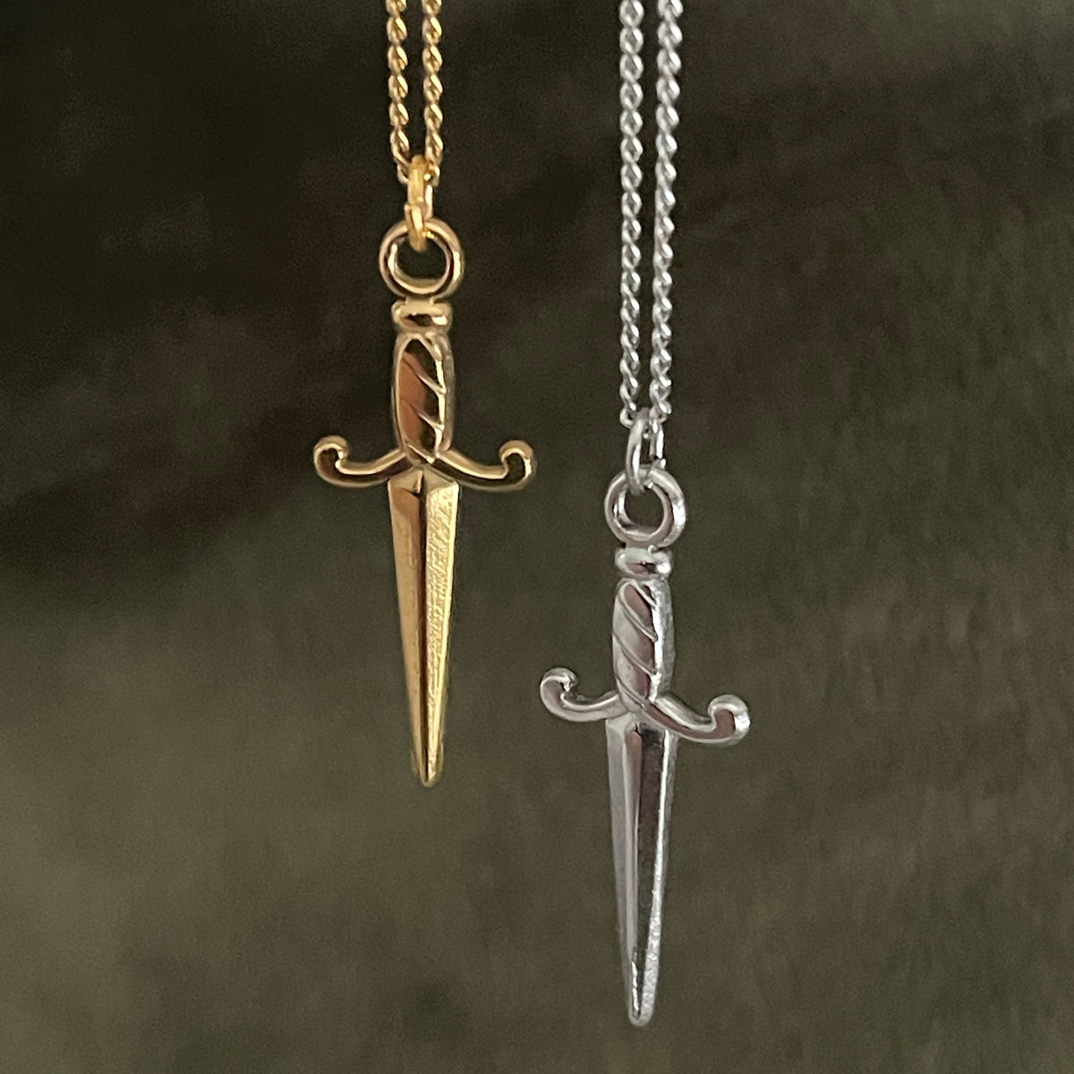 Gold and silver dagger-shaped pendants on chains against a dark background