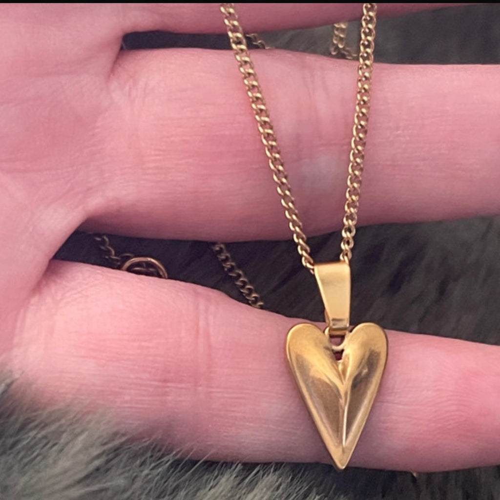 Gold heart-shaped necklace on a finger against a fur background