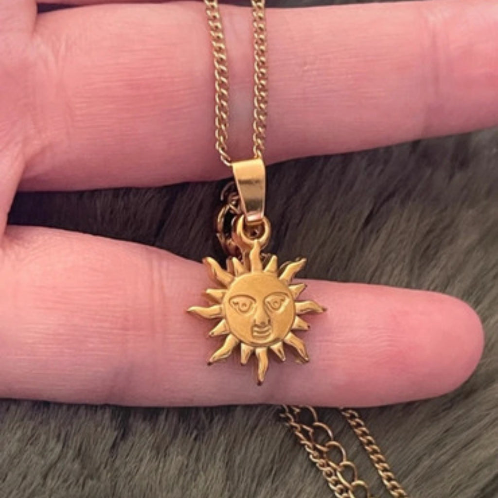 Gold sun-shaped pendant necklace held between fingers on a fur surface