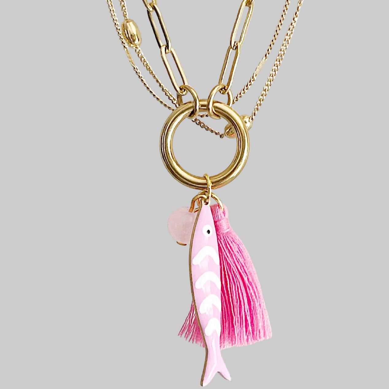 Gold necklace with a pink fish charm on a gray background