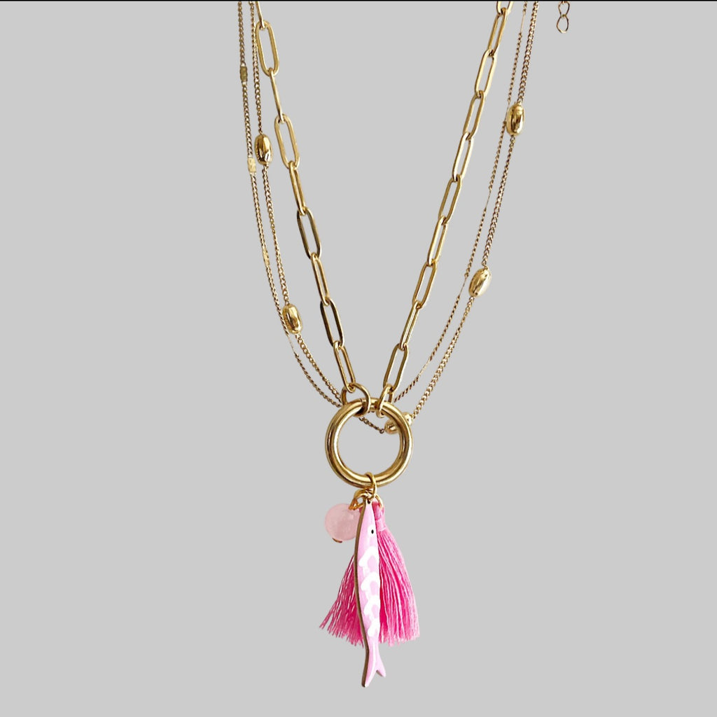 Gold chain necklace with a pink fish, bead and tassel on a grey background