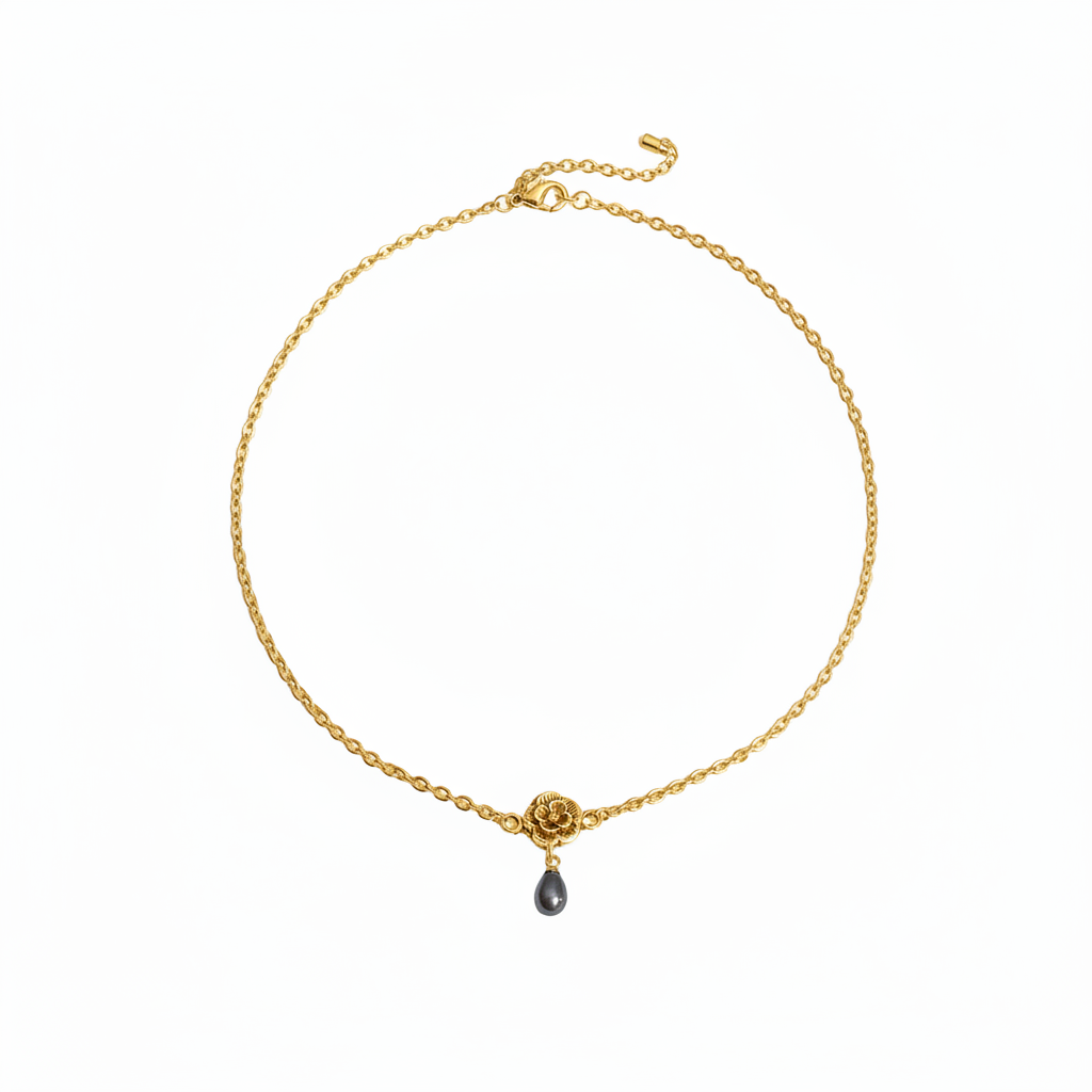 A delicate gold chain necklace featuring a small gold rose motif and a dangling dark gray teardrop gemstone, displayed on a clean white background.