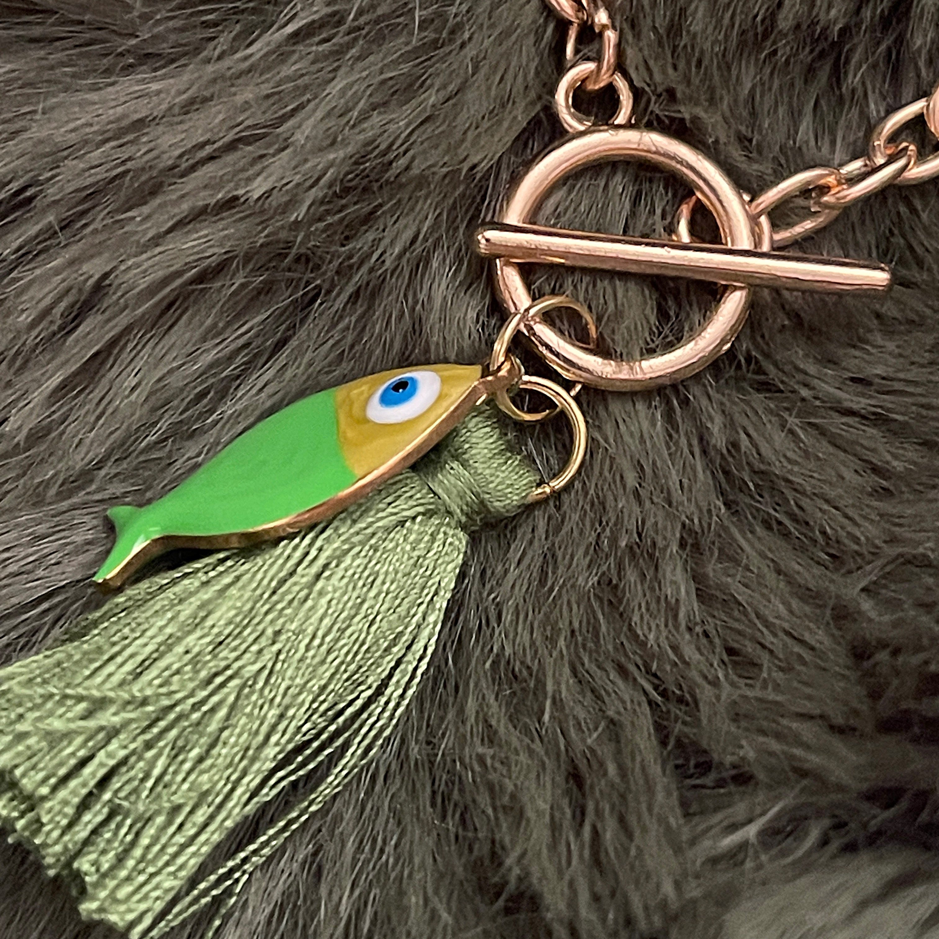 Gold bracelet with fish charm and green tassel on a fluffy background