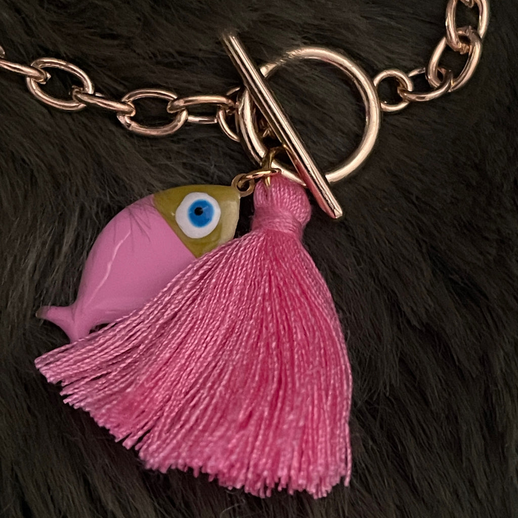 Pink fish charm with a tassel on a gold chain against a dark fur background