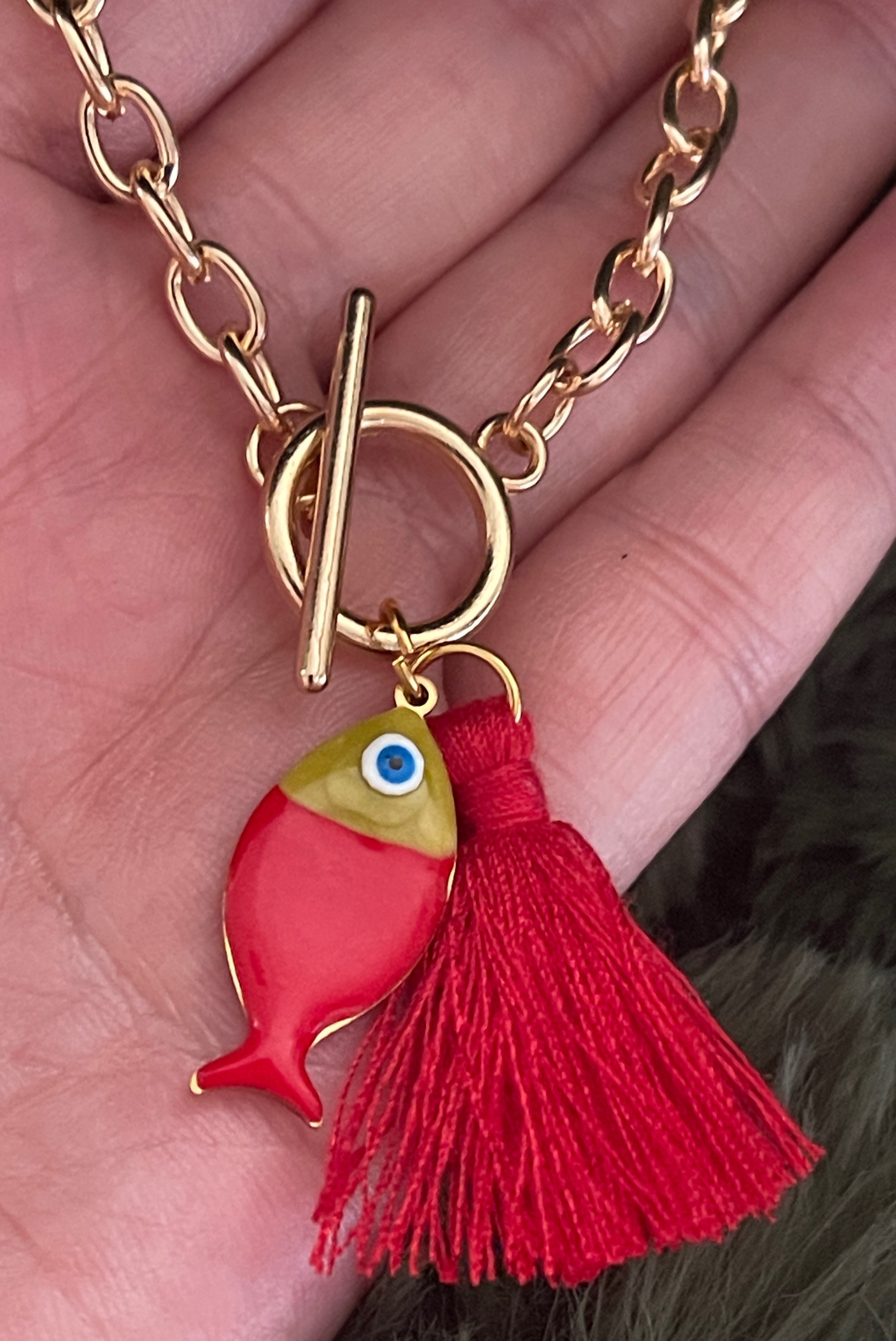 Gold bracelet with a red fish charm and tassel held in a hand.