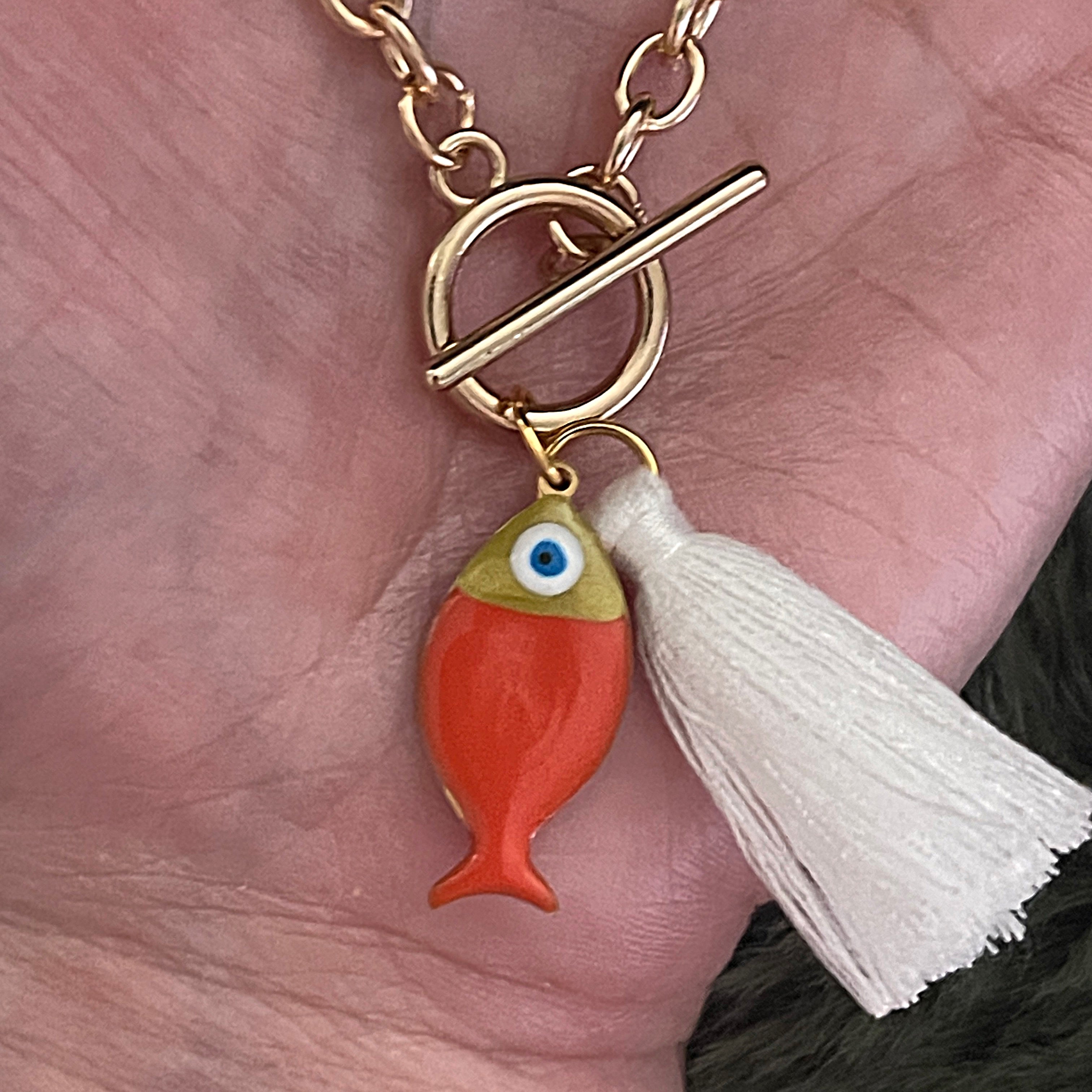 Gold bracelet with a fish charm and white tassel on a hand