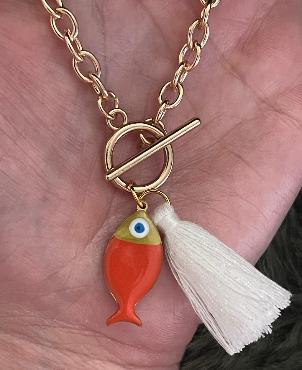 Gold bracelet with a fish charm and tassel held in a hand