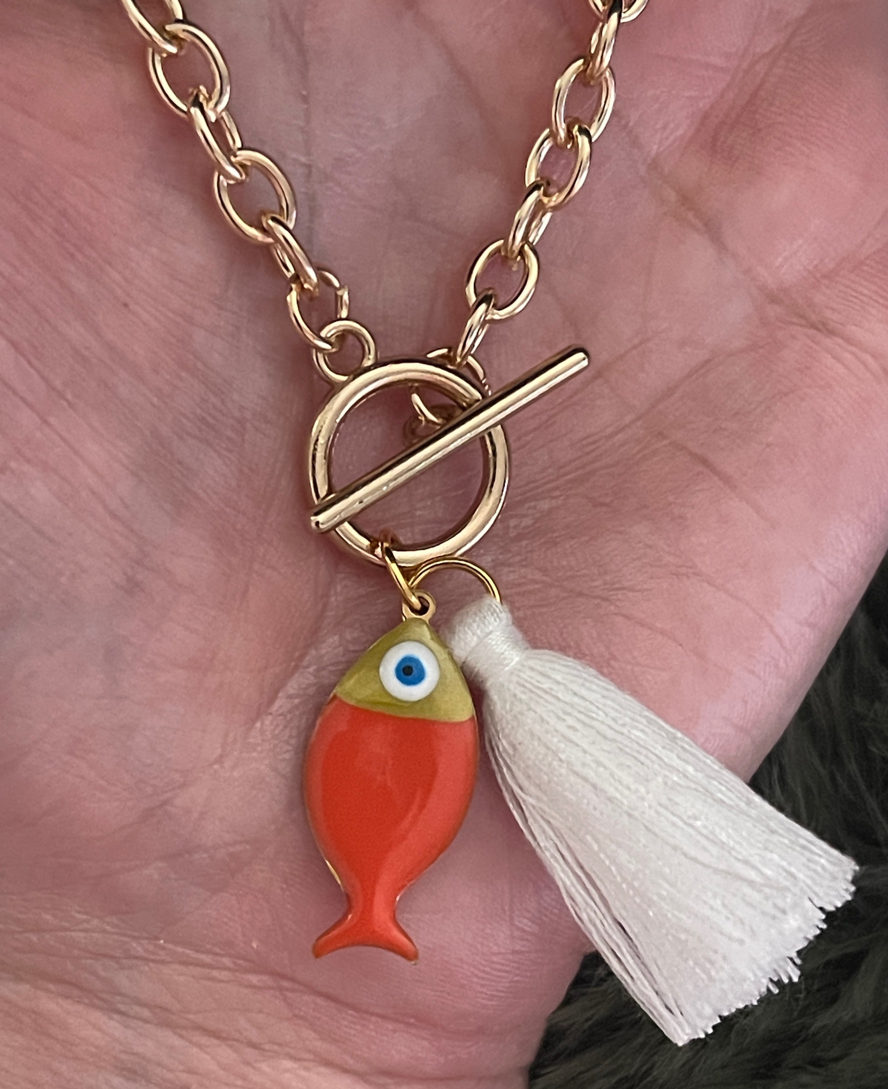 Gold bracelet with a fish charm and tassel held in a hand