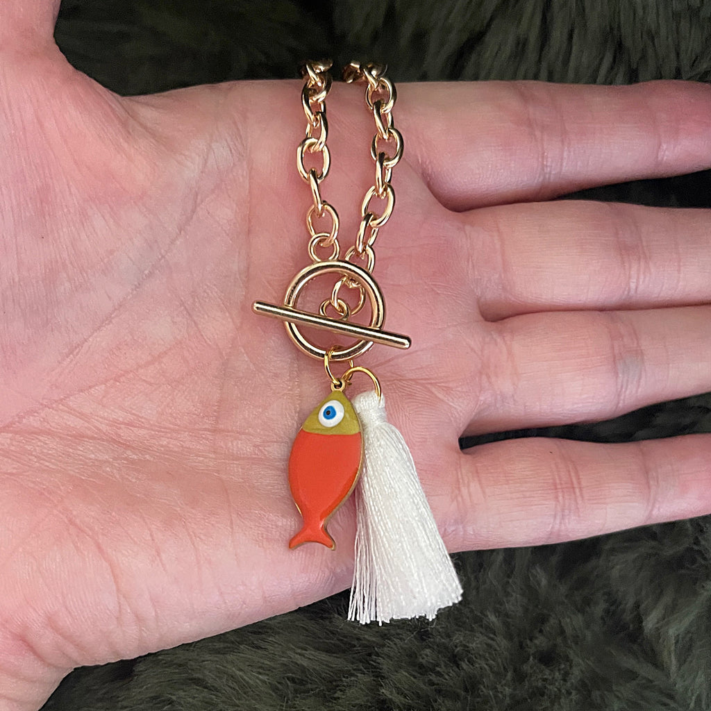 Gold chain bracelet with fish charm and tassel held in a hand.
