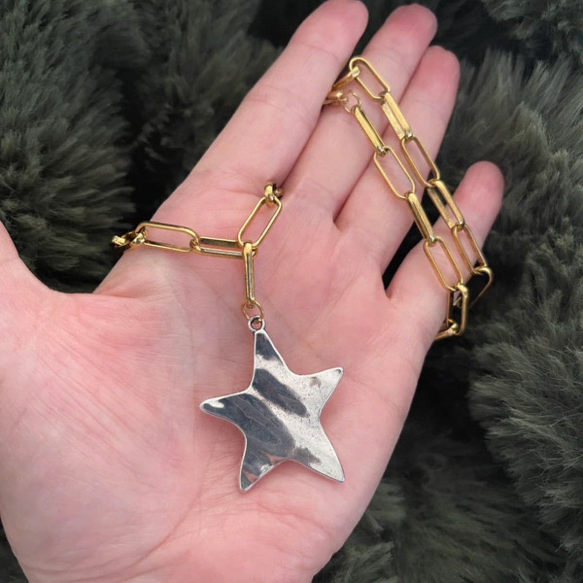 Hand holding a gold chain bracelet with a silver star pendant against a dark background
