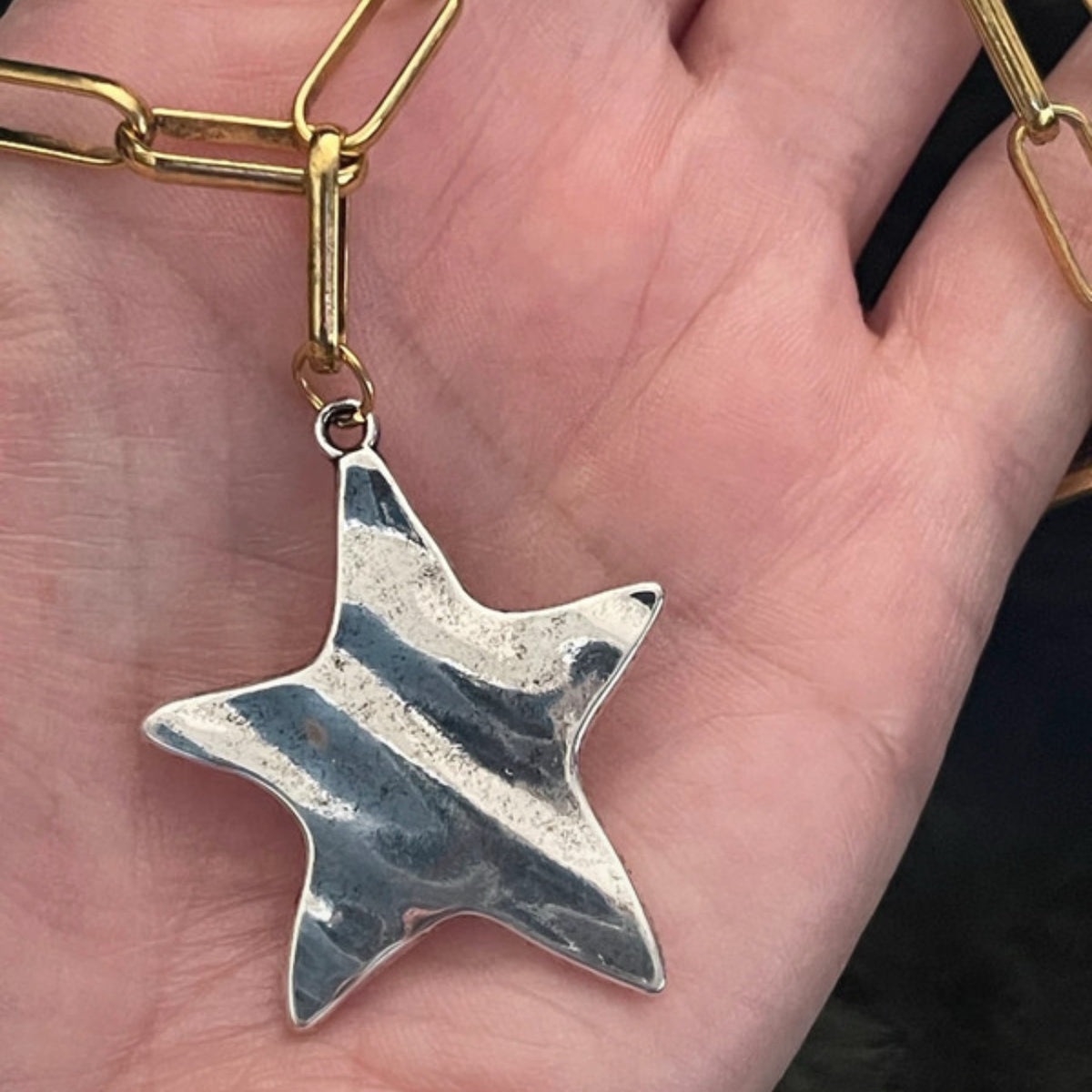 Silver star-shaped pendant on a gold chain held in a hand.