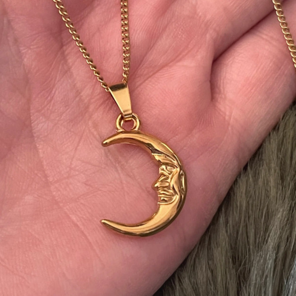 Gold crescent moon necklace with face design on a hand