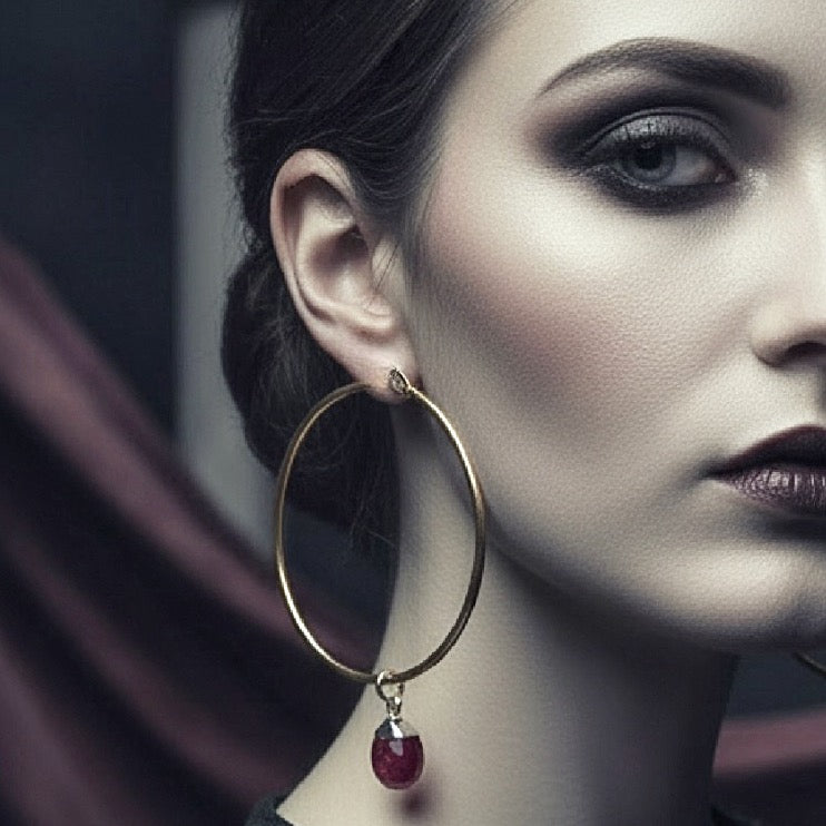 Close-up of a woman wearing a gold hoop earring with a red gemstone.