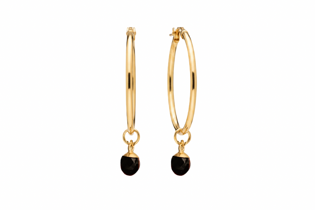 A pair of gold hoop earrings with a small oval black agate crystal against a white background