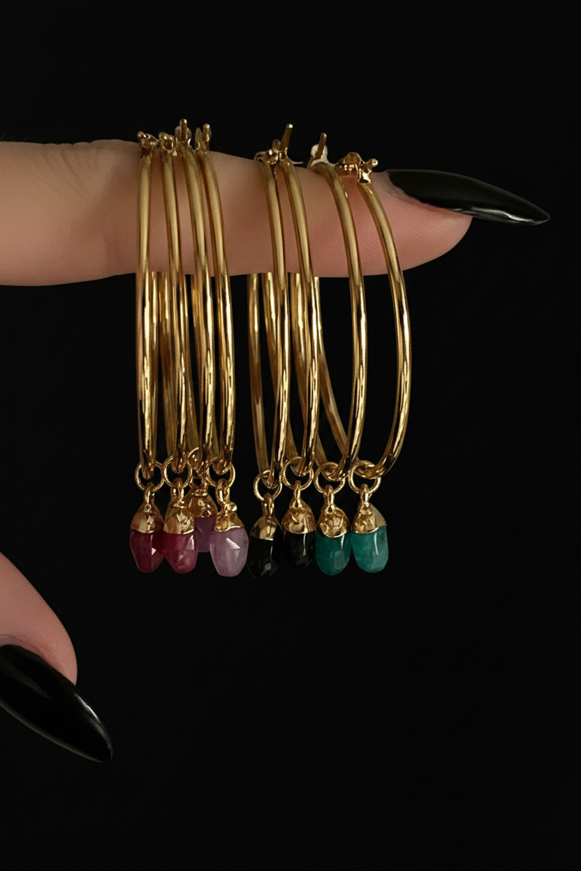 Gold bangles with gemstone drops on a black background