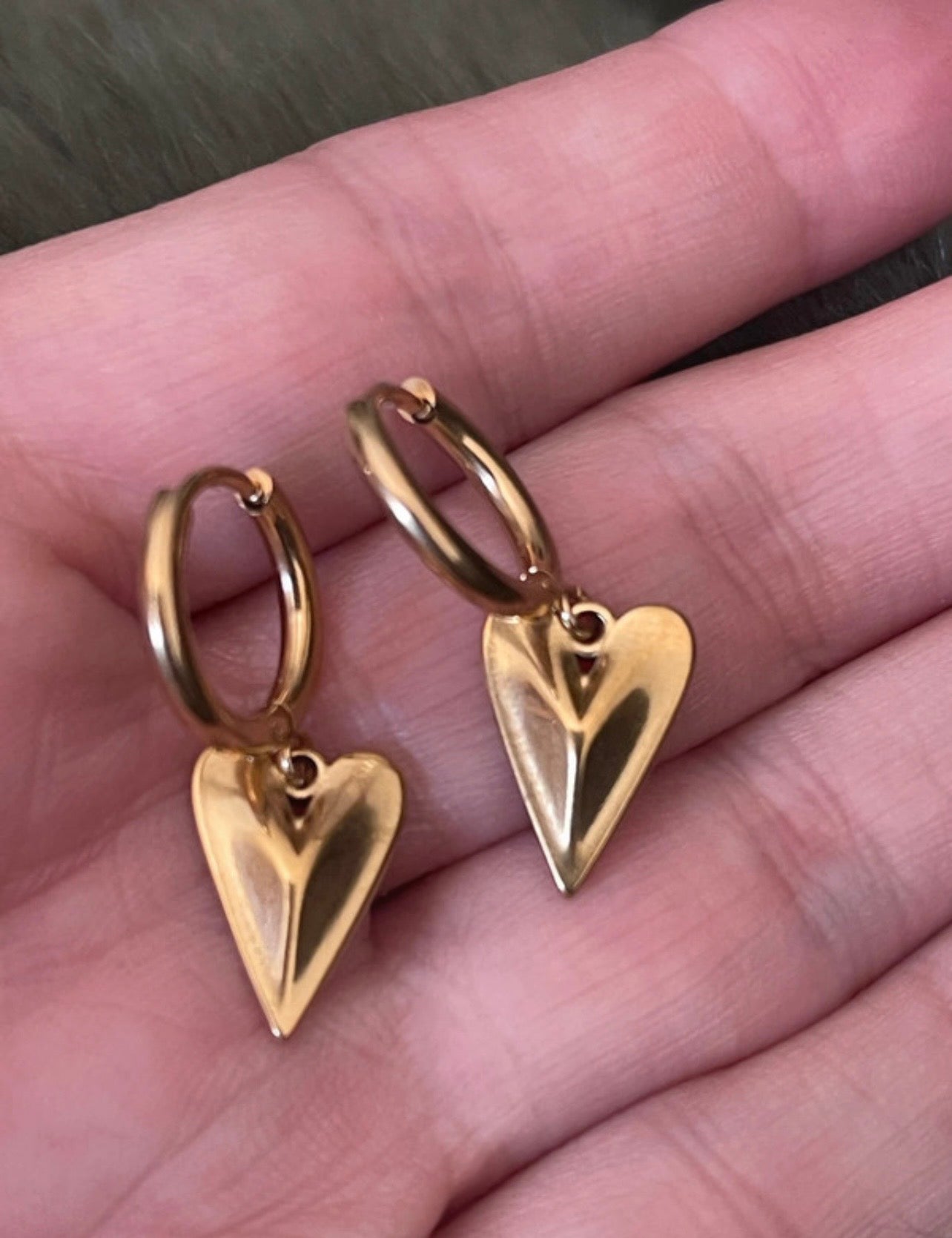Gold heart-shaped earrings held in a hand.
