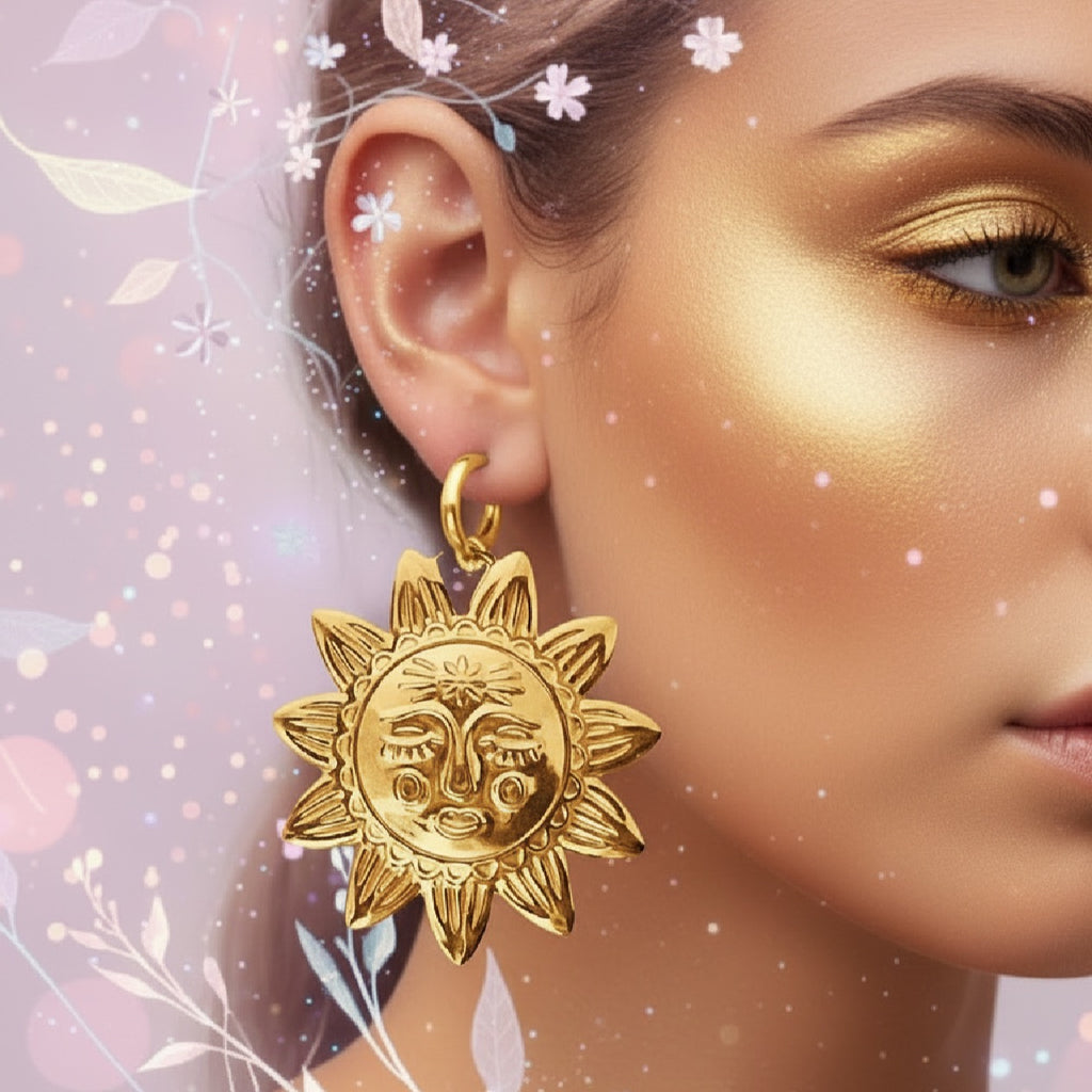 A close-up of a woman's ear and cheek wearing a dangling gold sun-face earring, with a soft pink floral background and sparkling decorative overlay.