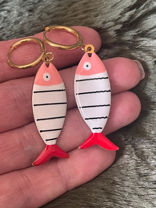 Two fish-shaped earrings with striped pattern held in a hand against a fur background