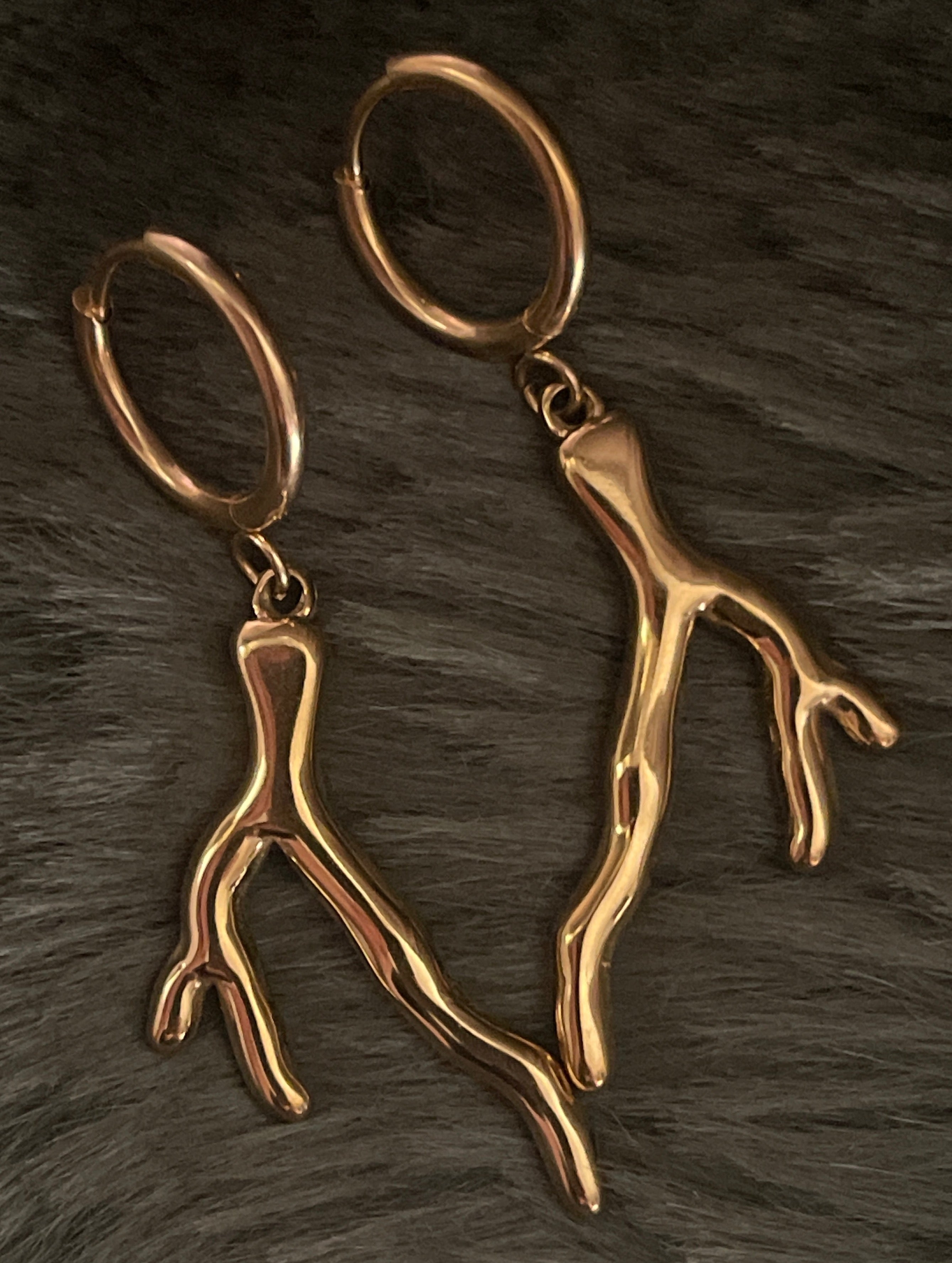 Gold coral-shaped earrings on a dark textured surface