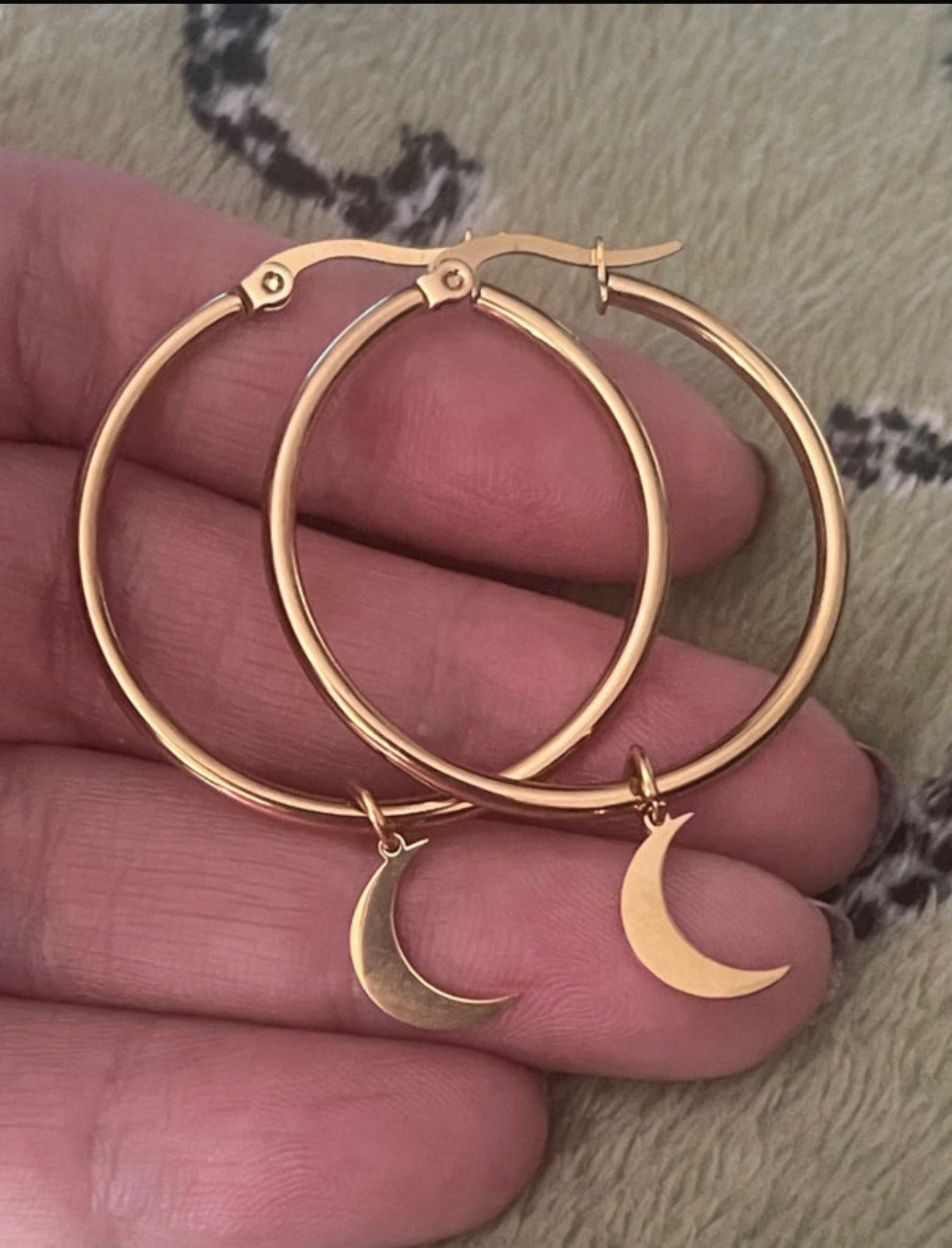 Gold hoop earrings with crescent moon charms held between fingers.