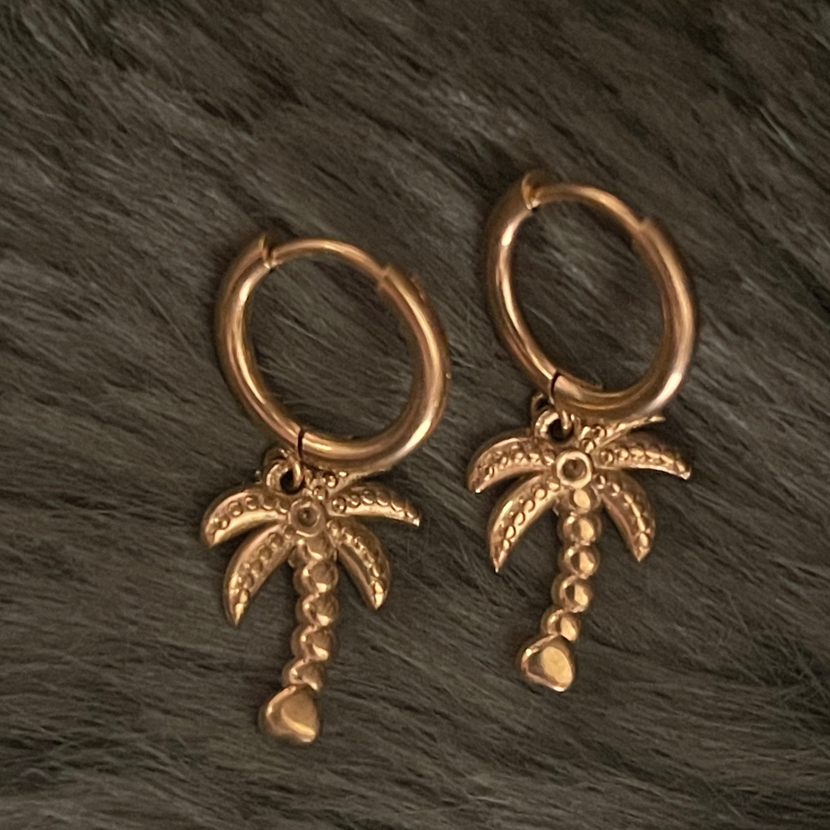 Gold hoop earrings with palm tree charms on a dark textured surface