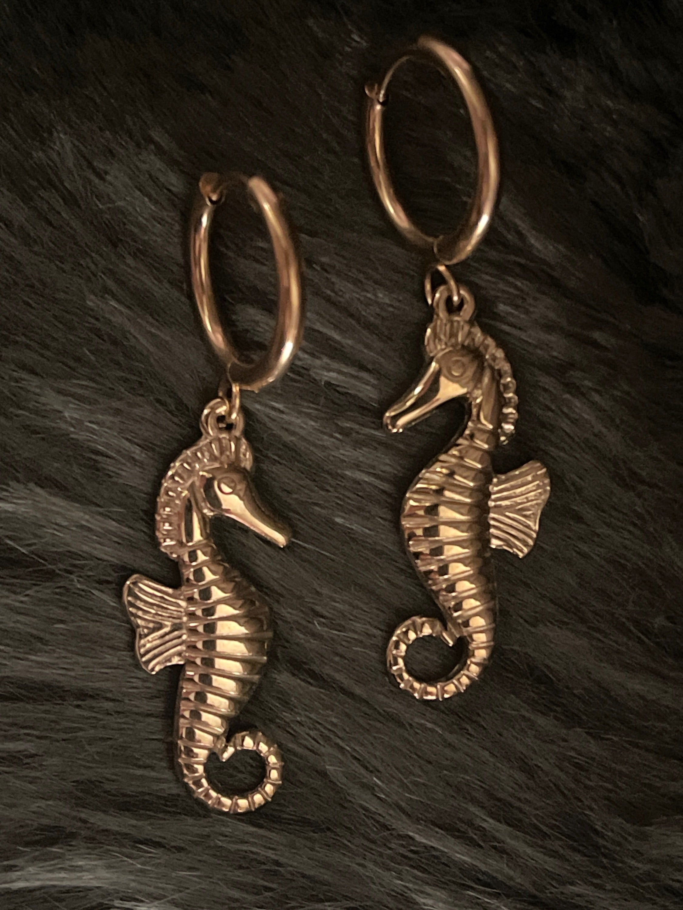 Gold seahorse earrings on a dark textured surface