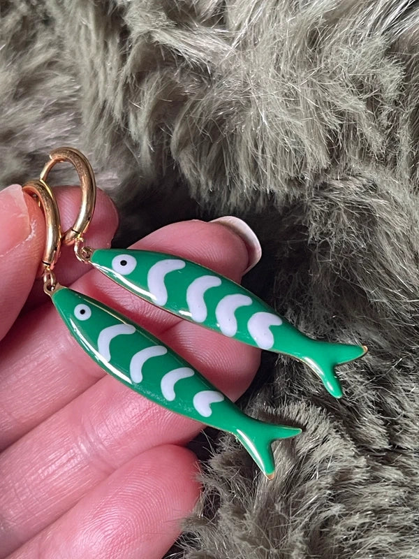 Green fish-shaped earrings held by a hand against a fur background