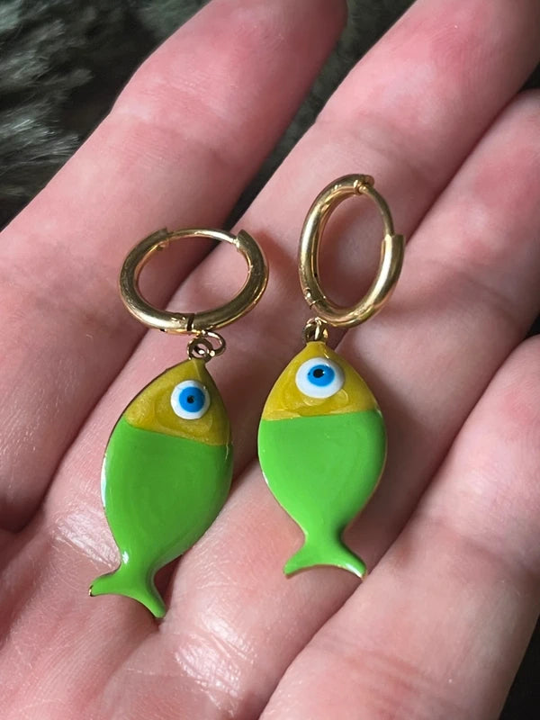 Green fish-shaped earrings with gold hoops on a hand.