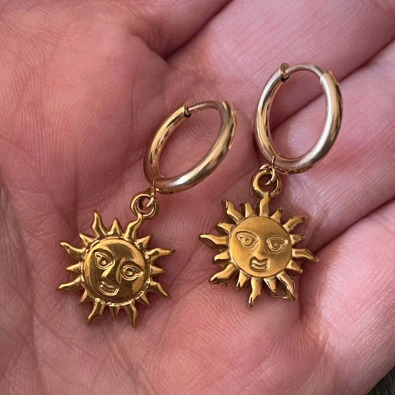 Gold sun-shaped earrings held in a hand