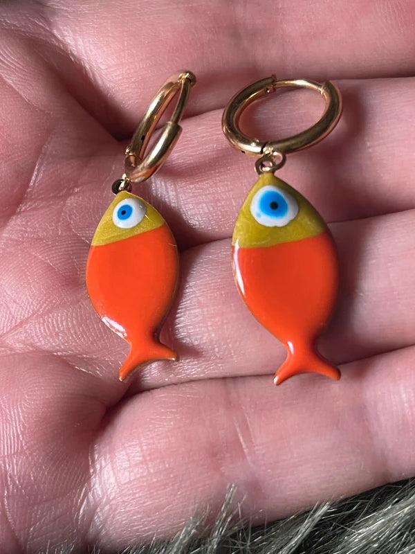 Orange fish-shaped earrings held between fingers.