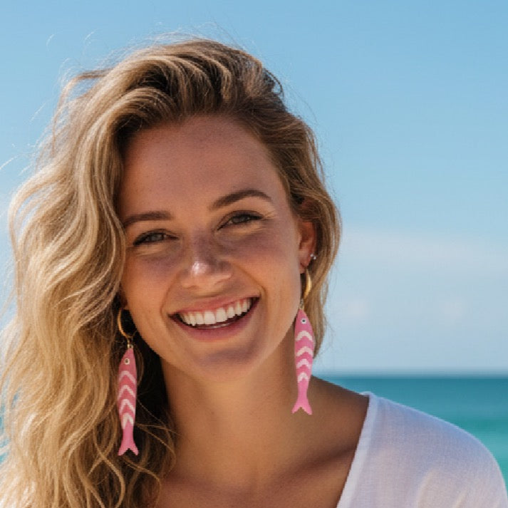 Woman wearing pink fish-shaped earrings with a clear blue sky background