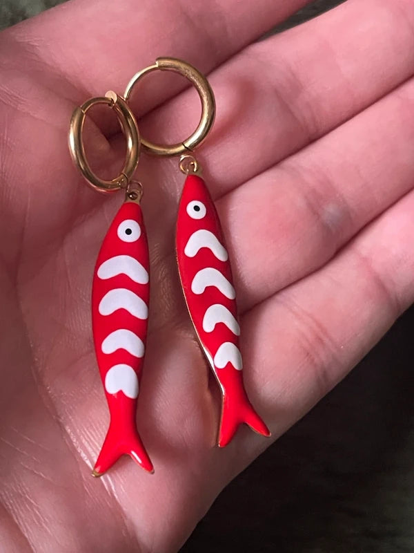 Red fish-shaped earrings with white patterns on a hand.