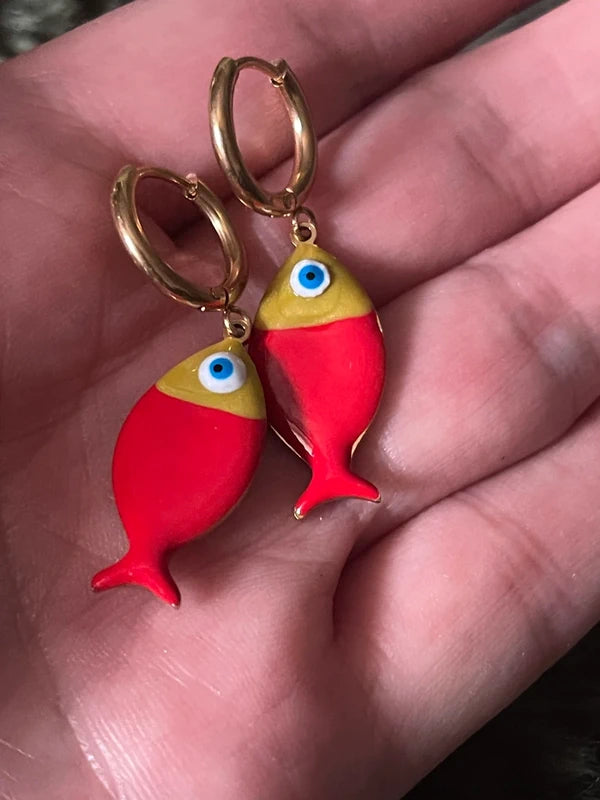 Red fish-shaped earrings with gold hoops held in a hand.