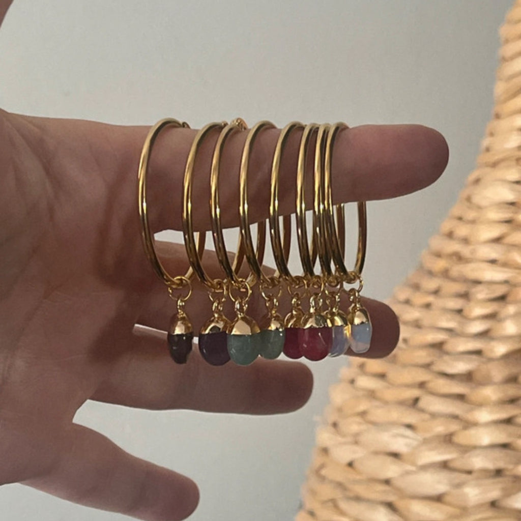 Gold hoop earrings with colourful drops on a hand against a neutral background