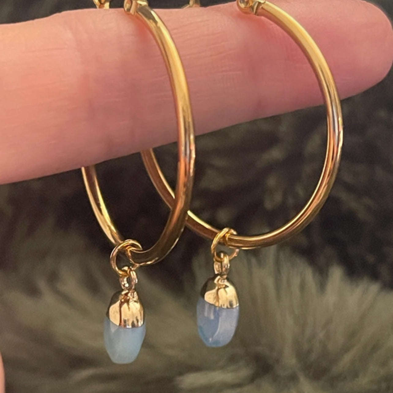 Gold hoop earrings with opal drop charms on a blurred background