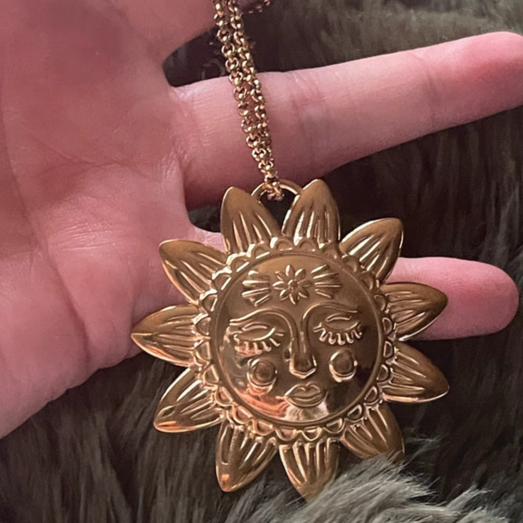 Gold sun-shaped pendant necklace held by a hand against a fur background