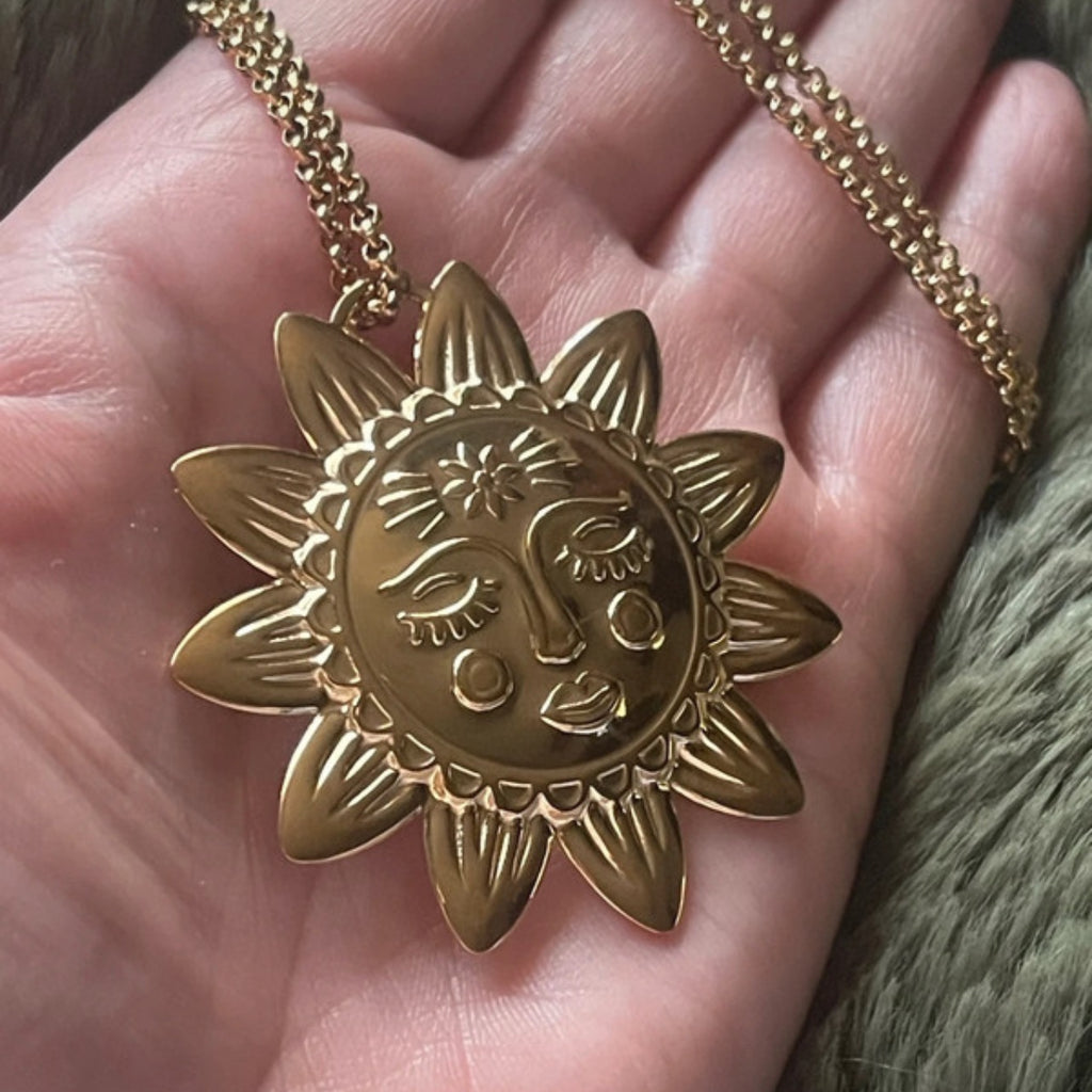 Gold sun and moon pendant on a chain held in a hand.