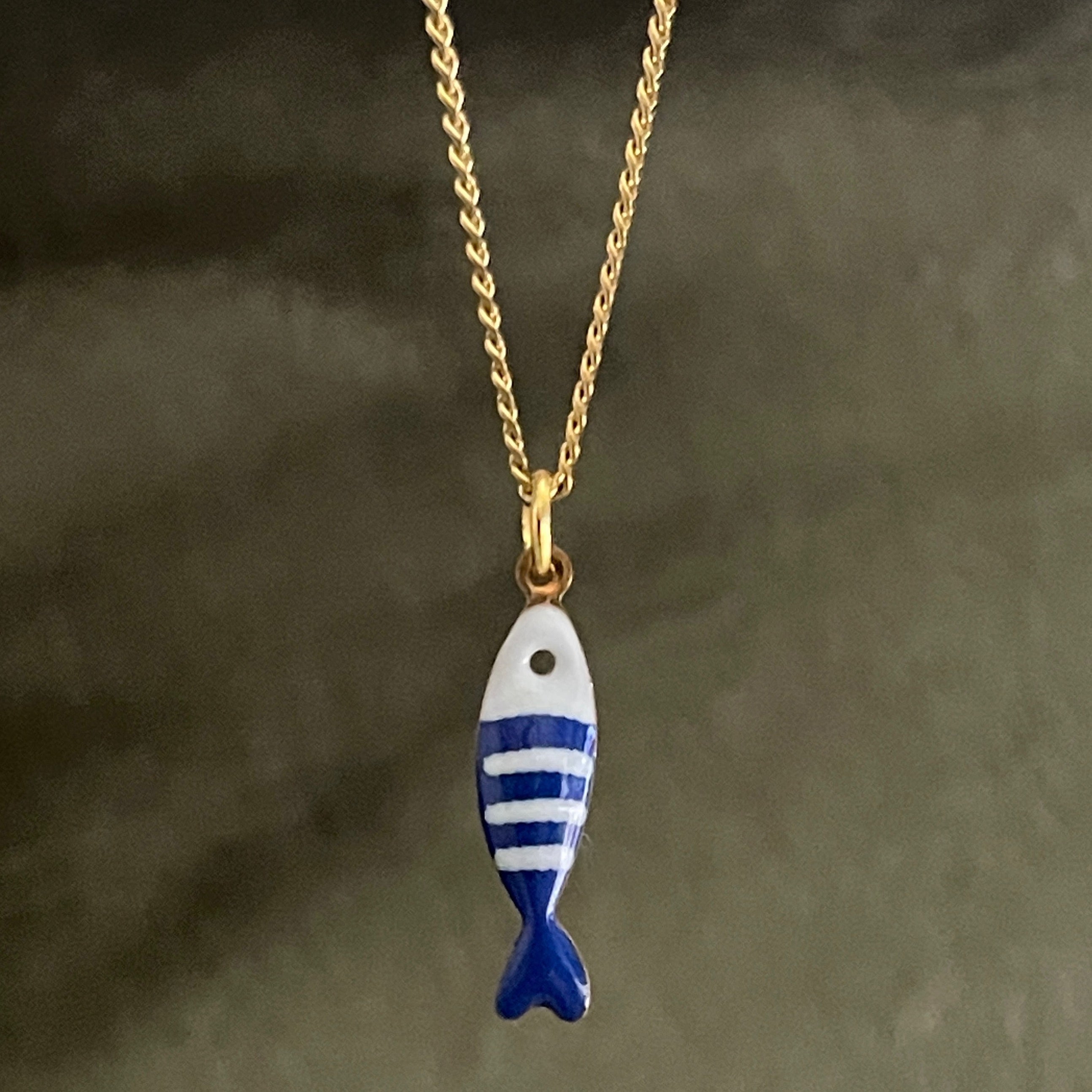 Fish-shaped pendant on a gold chain against a dark background