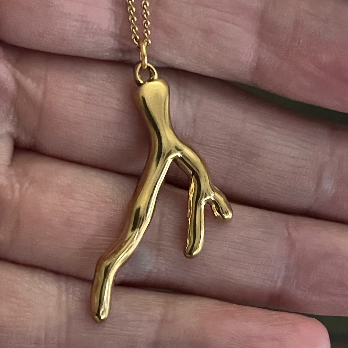 Gold coral-shaped pendant on a chain held in a hand.