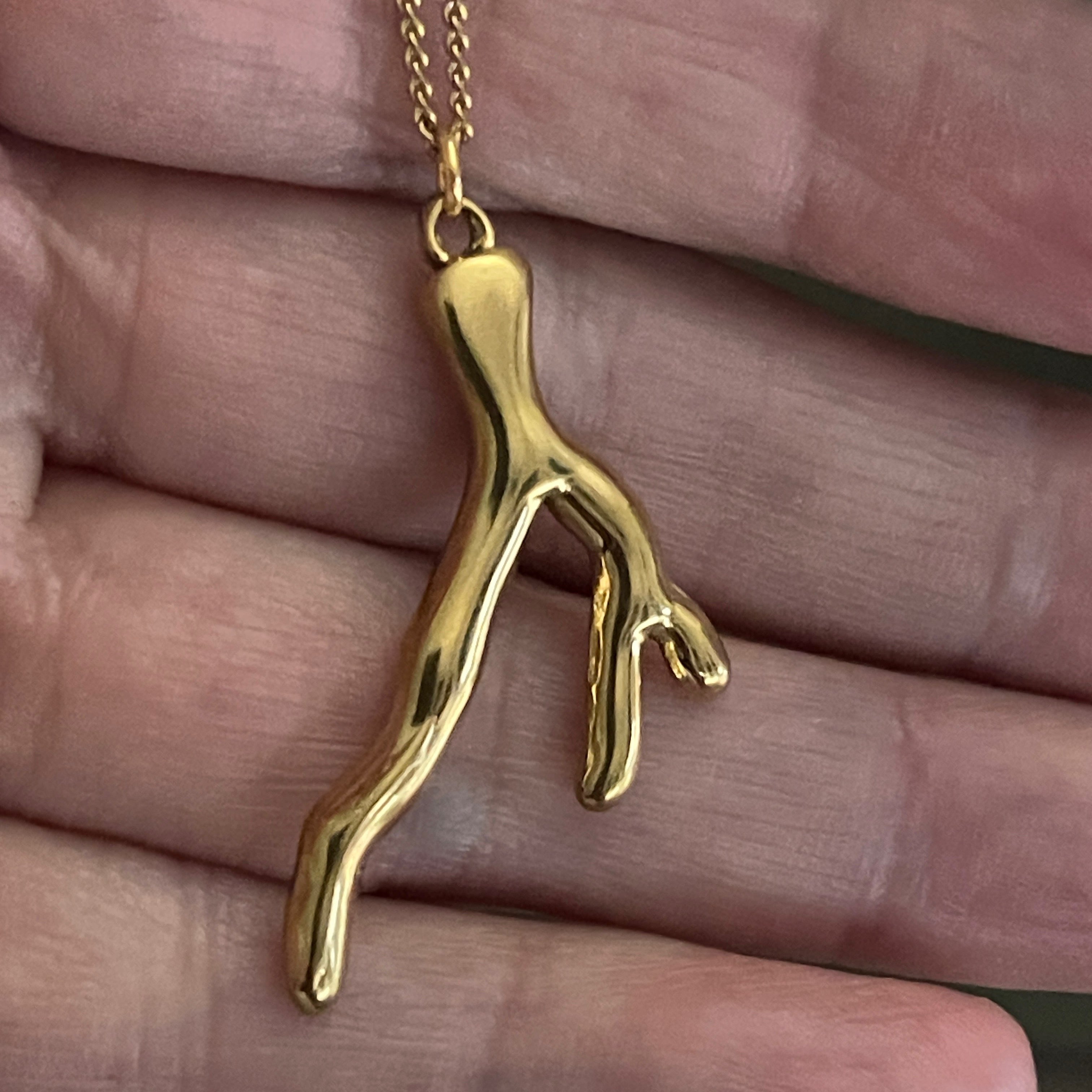Gold coral-shaped pendant on a chain held in a hand.