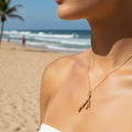 Close-up of a person wearing a gold necklace with a coral pendant on a beach.
