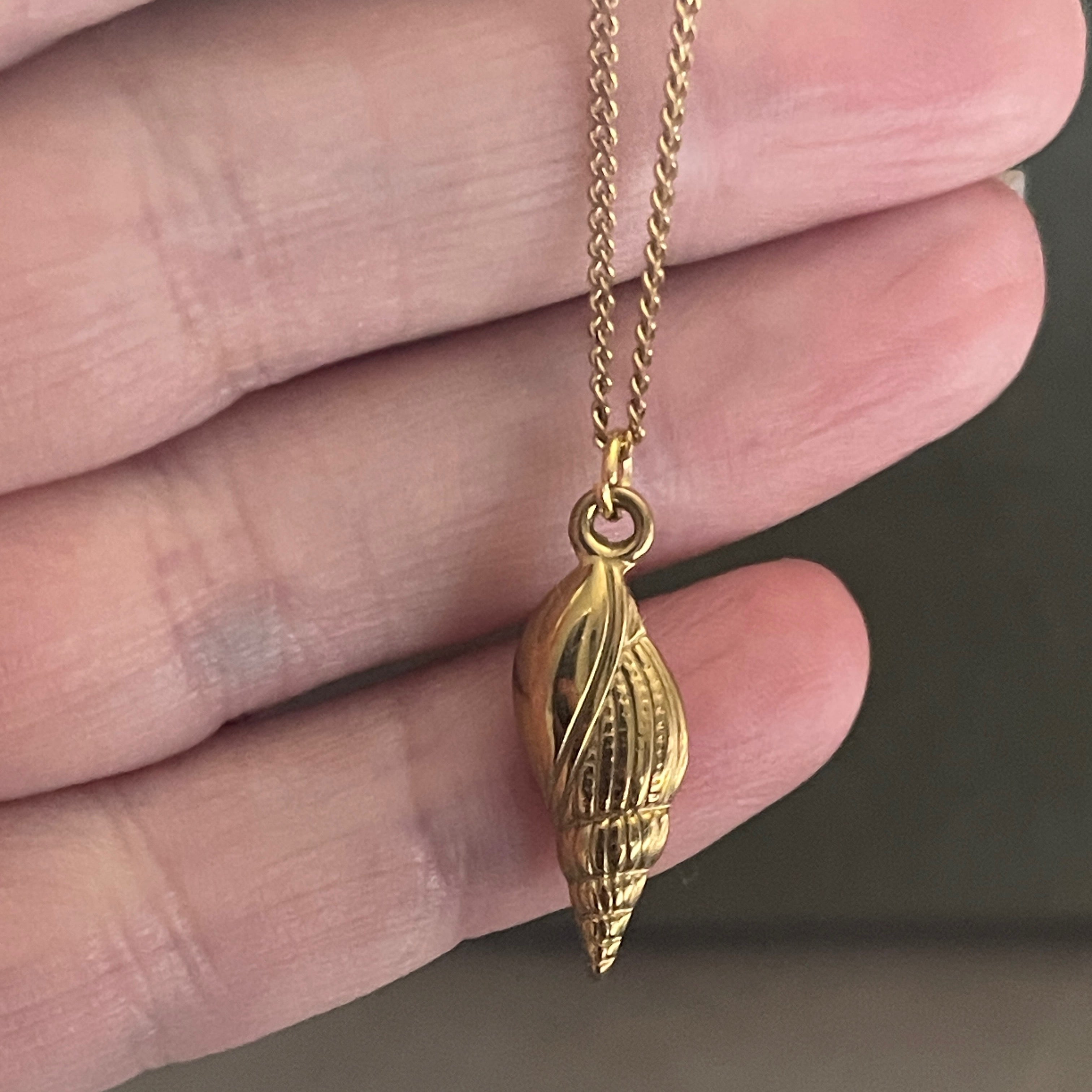 Gold shell pendant necklace held between fingers